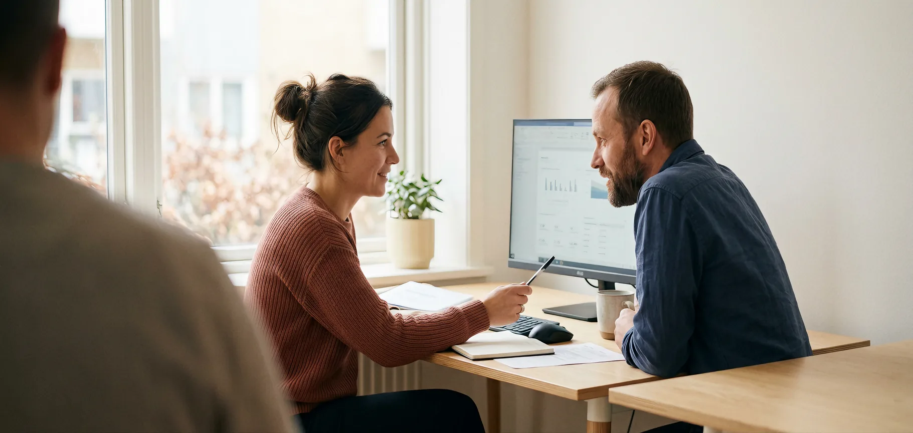 Two people at a shared desk reviewing something on a monitor together